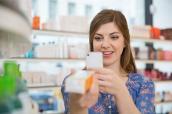 Frau fotografiert Medikament mit Smartphone in einer Apotheke.