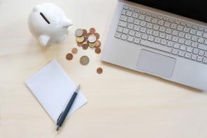 Laptop mit Sparschwein und Geldmünzen