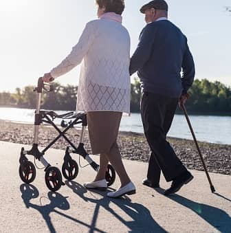 Seniorenpaar mit Rollator und Stock am Wasser