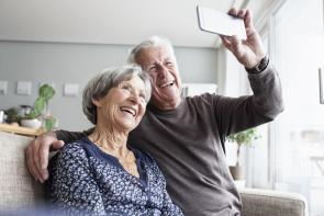 Senioren-Paar sitzt im Wohnzimmer auch Couch und macht ein Selfie.