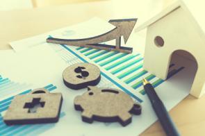 Kleine Sparsymbole und ein Holzhaus liegen auf ausgedruckten Statistiken