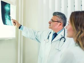 Arzt und Patientin schauen auf Röntgenaufnahme von Wirbelsäule.